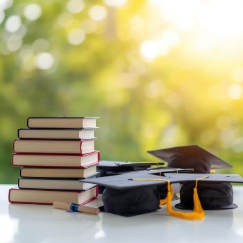 Books and graduation caps with a bright, sunny background